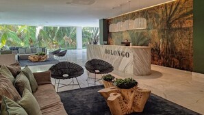 A modern hotel lobby with a reception desk labeled 'BOLONGO,' a seating area with sofas and chairs, and a large mural of tropical foliage. - Amazing Condo - Beach Access - Spa - Pool (Punta de Mita)