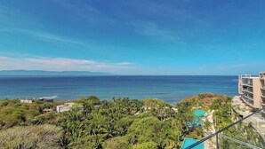 A coastal view with a clear sky, a body of water, and a building with balconies overlooking the sea. - Amazing Condo - Beach Access - Spa - Pool (Punta de Mita)