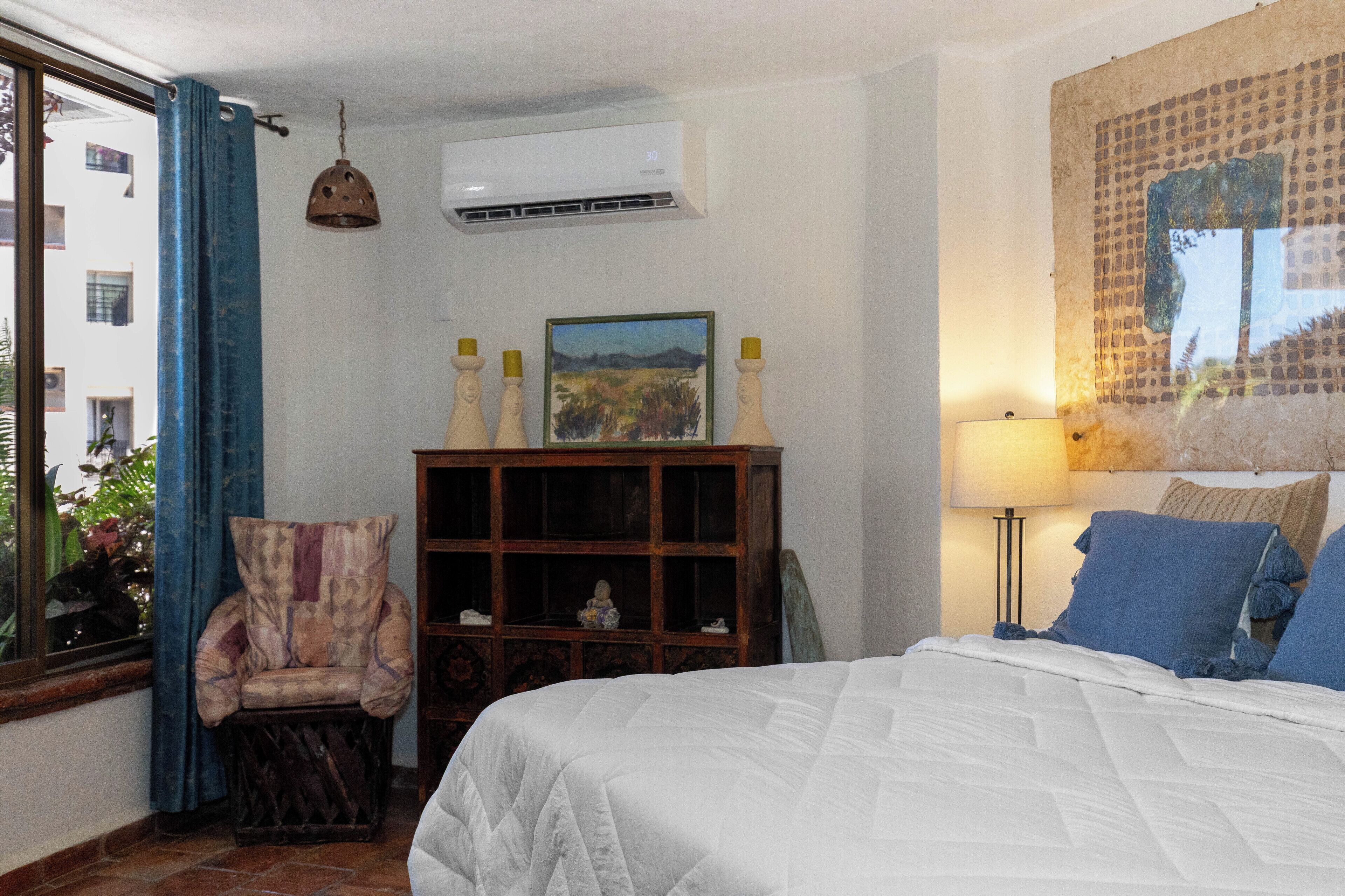 Un dormitorio con cama, una silla, un armario de madera, aire acondicionado y una lámpara de pared.