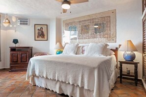 Une chambre avec un grand lit, un ventilateur de plafond, un climatiseur mural, une armoire en bois et un grand tableau abstrait.