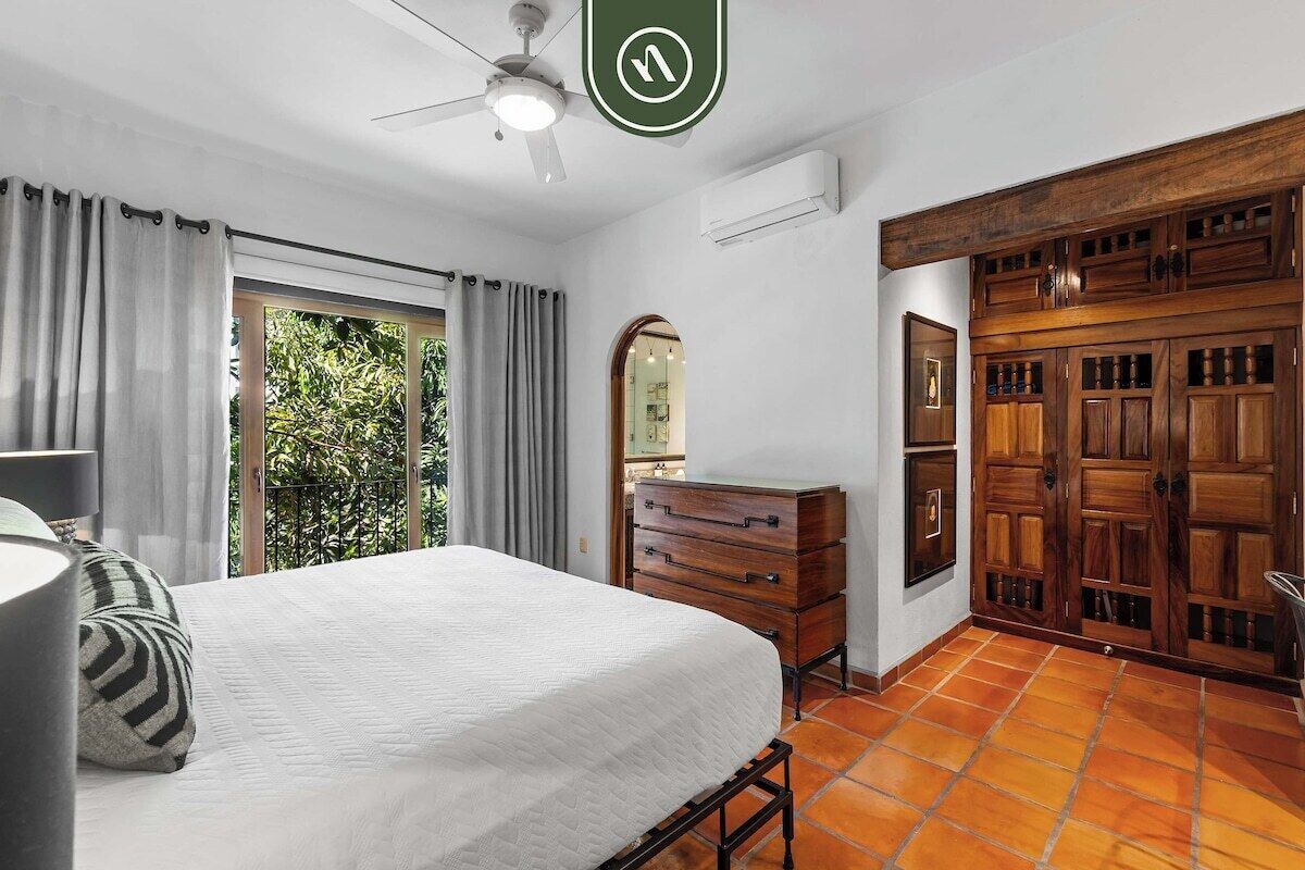 Une chambre à coucher avec un lit, une commode, un ventilateur de plafond et une vue sur la verdure à l’extérieur.
