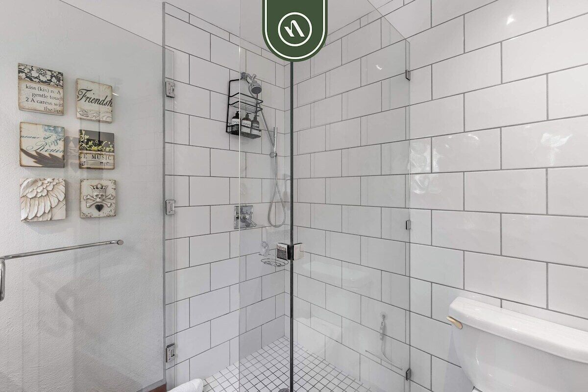 A modern bathroom with white tiles, a glass shower enclosure, and decorative wall art.