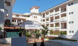 A multi-story building with balconies, a sign reading 'One Beach Street Valladolid,' and potted plants. - Amazing 1 BR Condo - Partial Oceanview - Pool (Puerto Vallarta)