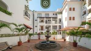 A courtyard with a central fountain, potted plants, and a bench. - Amazing 1 BR Condo - Partial Oceanview - Pool (Puerto Vallarta)