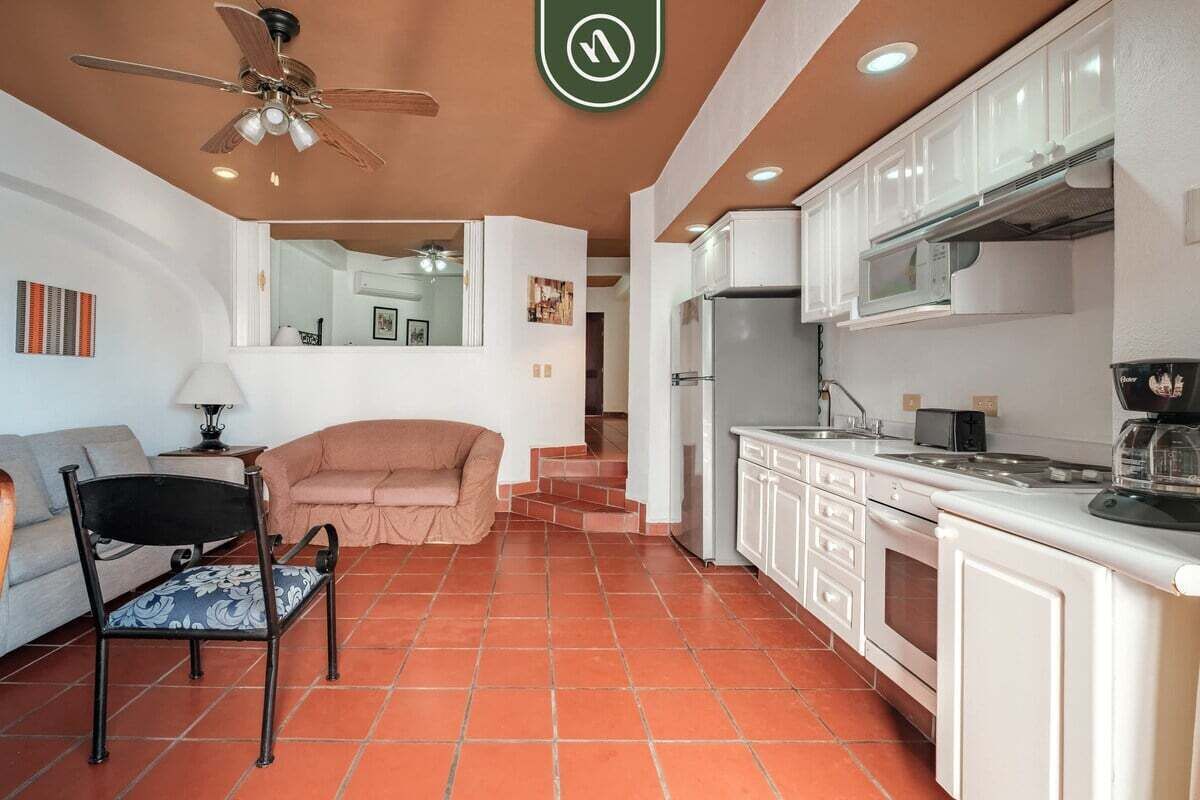 A compact living space with a kitchenette, a sofa, a chair, and a ceiling fan.