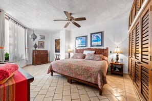 A hotel room with a bed, a ceiling fan, a nightstand with a lamp, and a wooden wardrobe.
