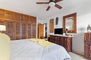 Une chambre d’hôtel avec un lit, une armoire en bois, une télévision et un ventilateur de plafond.