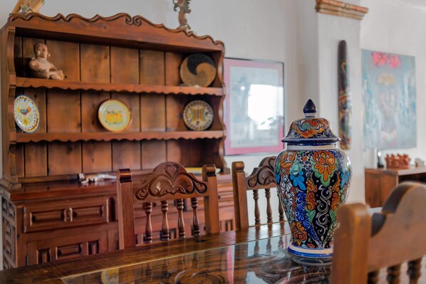 Una mesa de comedor con un jarrón de cerámica decorativo, sillas de madera y un mueble de madera con platos.