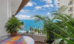 A balcony with a view of the ocean, potted plants, and a table with a colorful tablecloth. - Ocean View 2Br Condo-balcony-beach-pool - 902 (Puerto Vallarta)
