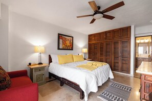 Un dormitorio con cama, armario de madera, lámparas de noche, ventilador de techo y un cuadro en la pared.