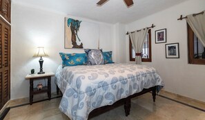 A bedroom with a bed, a nightstand, a lamp, a window with curtains, and a painting on the wall.