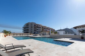 Une piscine sur le toit, agrémentée de chaises longues, un immeuble doté de nombreux balcons et une montagne en arrière-plan.