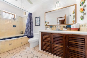 Un baño con bañera, inodoro, tocador con espejo y paredes con azulejos.