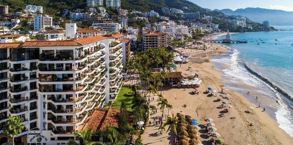 A coastal hotel with multiple balconies, a beach, and a view of the sea.