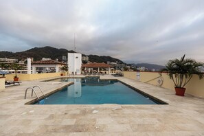 Una piscina en la azotea con vistas a un paisaje urbano y montañas al fondo.