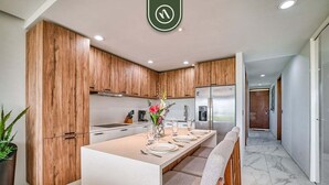 A modern kitchen with wooden cabinets, a central island, and a dining area. - 2BR Condo in Bucerias - Pickleball Court - Gym (Bucerías)