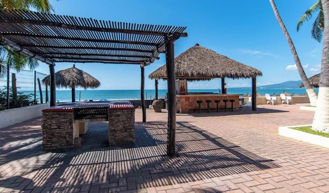 A beachside patio with a thatched-roof structure, a stone bench, and a bar area.