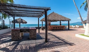 A beachside patio with a thatched-roof structure, a stone bench, and a bar area.