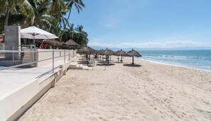Une plage avec une piscine, des parasols et des palmiers.