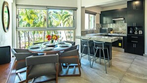 A modern kitchen with dark cabinets, a marble countertop, and a view of palm trees. - Beachfront 2BR Condo - Pool - Blue Flag Beach (Nuevo Nayarit)