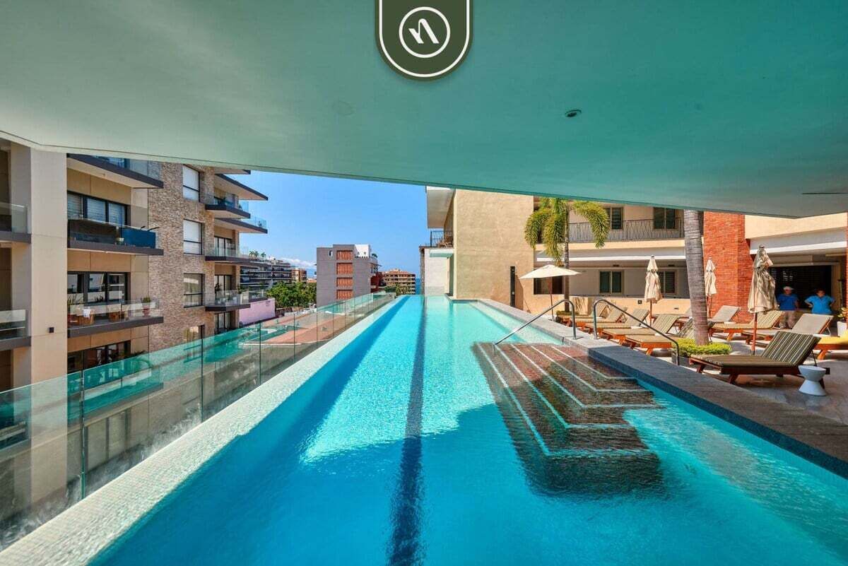 A modern hotel with a rooftop infinity pool, outdoor seating, and a view of the cityscape.