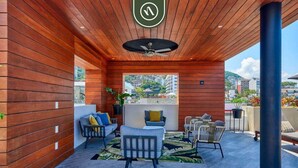 An outdoor patio with wooden panel walls, a ceiling fan, and seating areas with cushions.