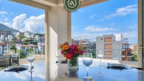 A round table with a vase of flowers, wine glasses, and cutlery, set against a cityscape view.