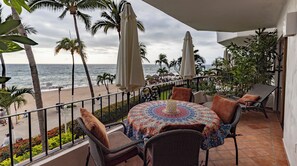 A balcony with wicker chairs, a patterned tablecloth, and a view of the ocean.