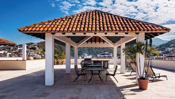 A covered outdoor seating area with a tiled roof, a table, chairs, and potted plants. - Ocean View 2Br Condo-balcony-beach-pool - 212 (Puerto Vallarta)