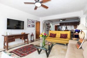 A living room with a sofa, coffee table, TV, wooden desk, and a ceiling fan. - Ocean View 2Br Condo-balcony-beach-pool - 212 (Puerto Vallarta)