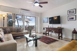 A living room with a sofa, coffee table, TV, and a view of the ocean. - Ocean View 2Br Condo-balcony-beach-pool - 212 (Puerto Vallarta)