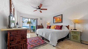 A bedroom with a bed, a ceiling fan, a nightstand, a dresser, a window with a view, and a door leading to an outdoor area. - Ocean View 2Br Condo-balcony-beach-pool - 212 (Puerto Vallarta)