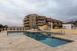 Une piscine sur le toit, dotée de chaises longues et d’un petit pavillon, le tout entouré d’immeubles à plusieurs étages.