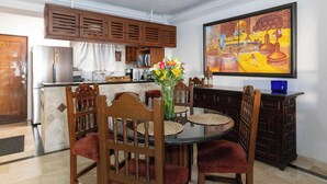 A dining area with a round table, wooden chairs, a vase with flowers, and a kitchen in the background. - Ocean View 2Br Condo-balcony-beach-pool - 212 (Puerto Vallarta)
