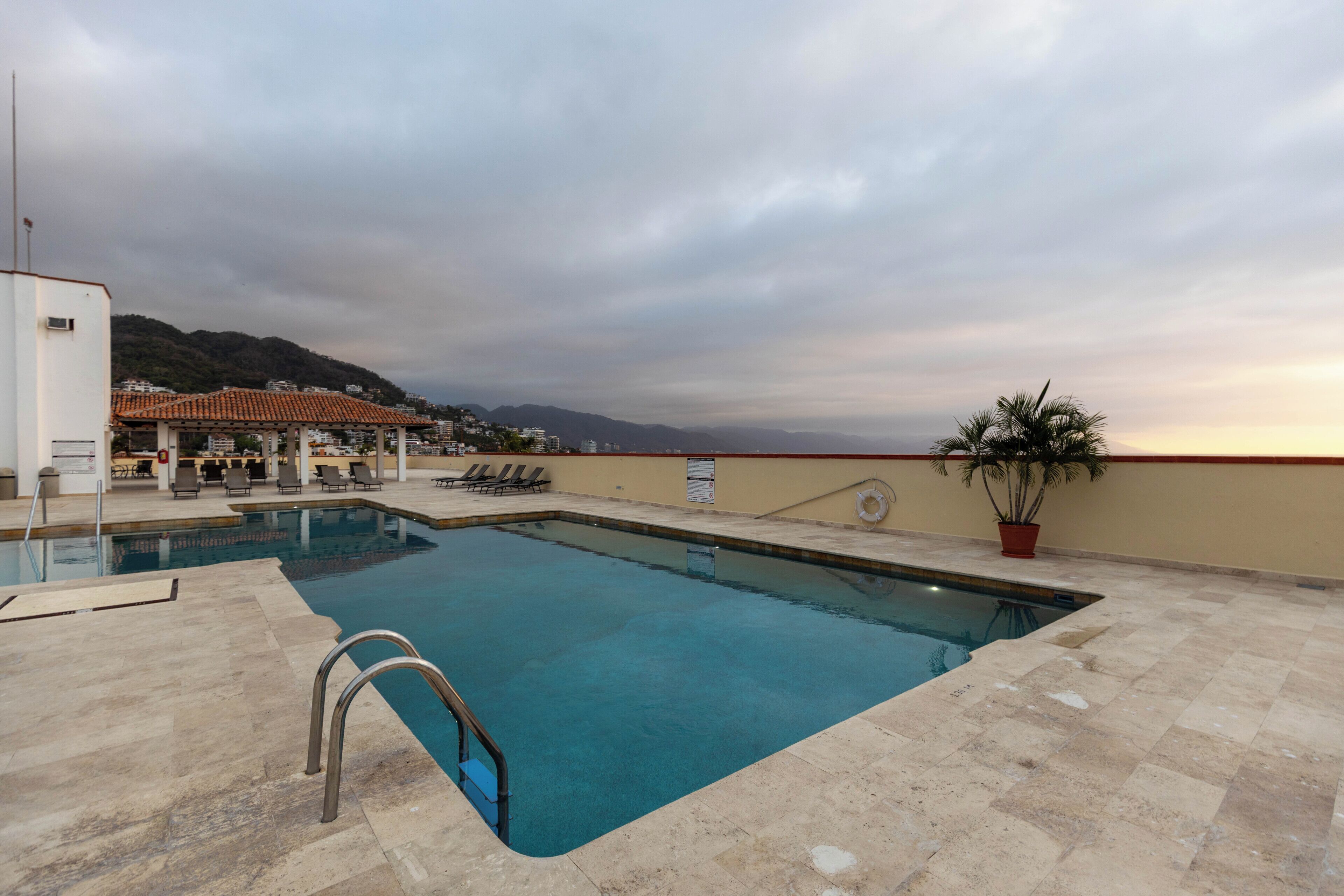 Piscina con vistas a montañas, zona de estar cubierta y una planta en maceta.