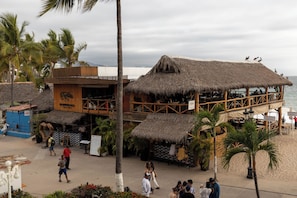Un restaurante en la playa con techo de paja, mesas al aire libre y vistas al océano.