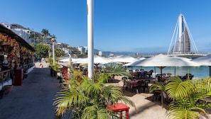 Un café frente al mar con terraza, vista al océano y una estructura de puente característica al fondo.