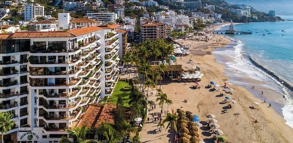 A coastal hotel with multiple balconies, a beach, and a pier.