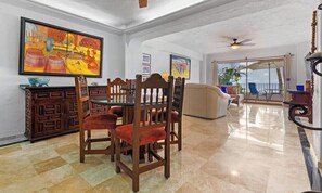 A dining area with a table and chairs, a painting on the wall, and a view of the outdoors.