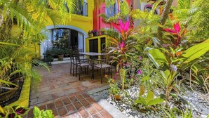 A courtyard with a table and chairs, surrounded by potted plants and a yellow building.