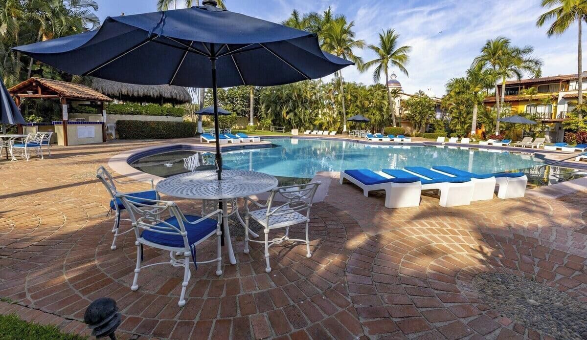 A pool area with lounge chairs, a table, and umbrellas.