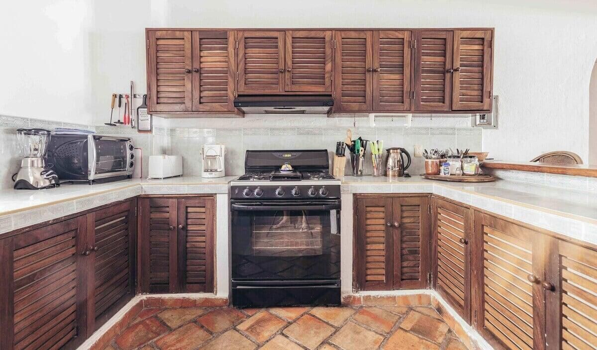 Een keuken met houten kastjes, een fornuis, een broodrooster en een blender.