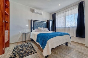 Une chambre à coucher comprenant un lit, une table de chevet, une commode, une fenêtre avec des rideaux et une armoire en bois.