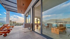 A modern outdoor lounge area with a pool table, lounge chairs, and a view of a cityscape and mountains.