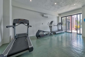 Une salle de sport équipée de tapis de course et d’un vélo d’appartement, dotée de grandes fenêtres et d’un sol en béton.