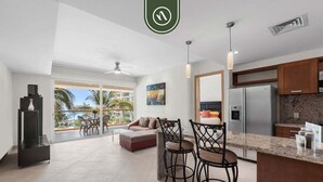 Una cocina moderna con refrigerador, comedor con taburetes de bar y un amplio ventanal con vista a palmeras.