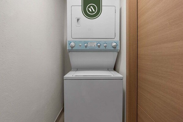 A compact, white washing machine with a control panel featuring four knobs and a green circular logo.