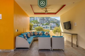 A modern hotel lobby with a curved sofa, a ceiling fan, and a view of surrounding buildings. - Amazing 1 BR Condo - Rooftop Pool - Bay View (Puerto Vallarta)