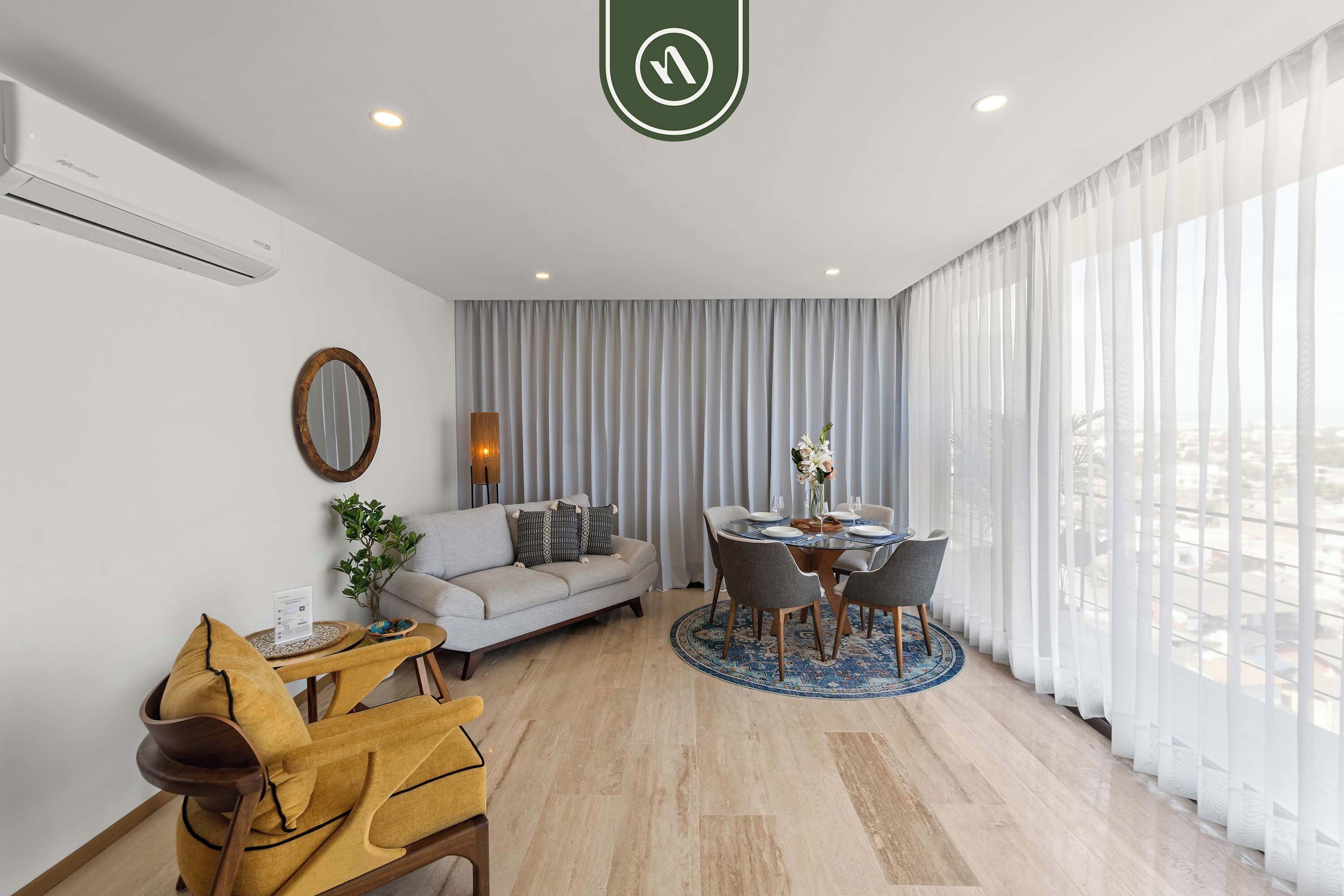 Een moderne woonkamer met een bank, een eettafel met stoelen en een groot raam met dunne gordijnen.