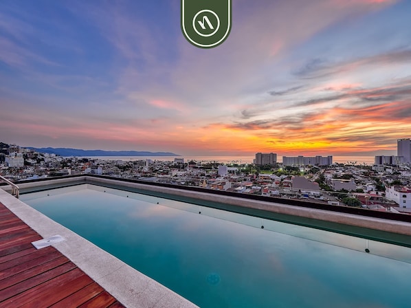 A rooftop pool with a cityscape view at sunset.